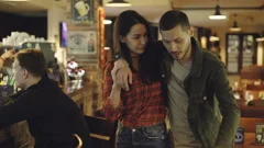 Dolly shot of young woman helping her drunk boyfriend leave bar. Handsome
