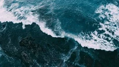 Abstract aerial view of moody ocean waves crashing on rocky shoreline