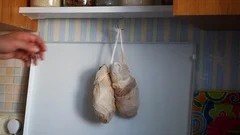 The man takes off the chicken legs hung from the stove above the stove, wrapp