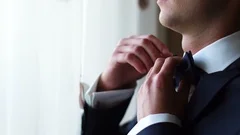 Side close-up view of the hadsome calm groom adjusting his blue bow-tie near the