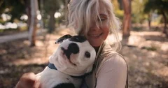 Smiling senior woman hugging pet dog in park in autumn