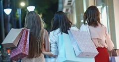 Backview of three female friends walking near mall with shopping bags in hands