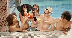 Five friends are having fun in swimmomg pool, chatting, and drinking cocktails