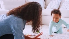 Black toddler boy crawling around his kneeling young mother