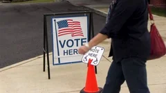 People walk by vote here sign with American flag and wheelchair