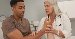 Close up of african-american male talking to mature doctor about arm injury