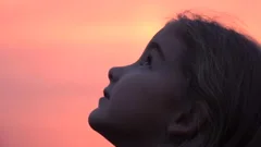 Kid looking up at the sky in nature. Little girl praying looking up at purple