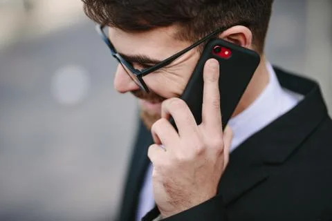 Close up of smiling businessman talking on smartphone. Happy male business professional making a phone call. xkwx business, businessman, caucasian, closeup, corporate, eyeglasses, face, happy, headshot, lifestyles, male, man, mobile, office, one, outdoors, people, person, phone, positive, professional, side, smartphone, smiling, standing, talking, technology, using, view, young
