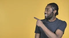 Casual African Man Pointing with Finger on Side, Yellow Background