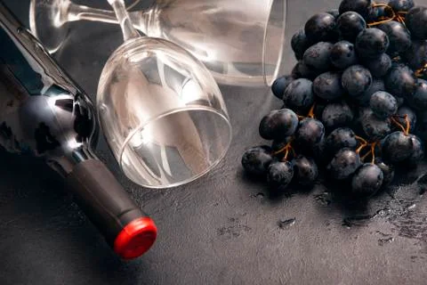 1 bottle of wine,  bunch of dark grapes, 2  empty glass, rose on a dark backg Stock Photos