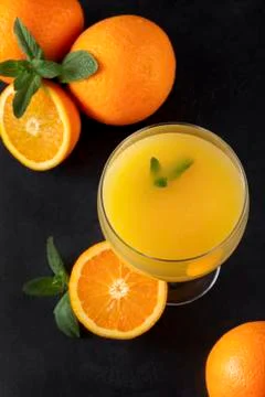 1 glass of orange juice with mint, fresh whole and half oranges on a black ba Stock Photos
