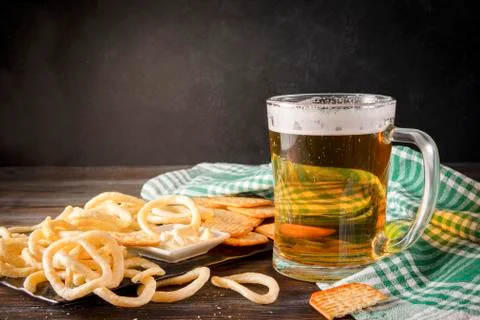1 mug of light beer with cracker, onion rings and sauce, checkered green towe Stock Photos