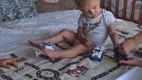 A 1 or 2 year old child plays with a screwdriver and siblings sitting on the bed Stock Footage 274632540