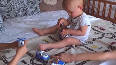 A 1 or 2 year old child plays with a screwdriver and siblings sitting on the bed Stock Footage 274639433
