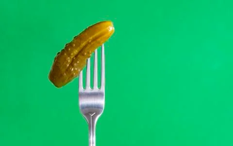 1 pickle, pickled cucumber with a fork on a  green background, vegetables Stock Photos