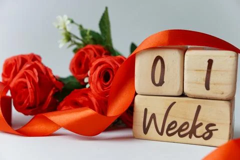 1 week gestational age milestone written on a wooden cube with red roses Stock Photos