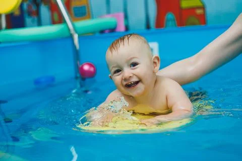 A 1-year-old boy learns to swim in a children's pool with a coach. Swimming.. Stock Photos