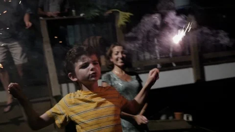 10 -11 year old boy playing with fireworks and sparklers with family in yard Stock Footage 90736287