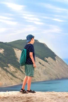 A 10-year-old boy with a backpack looks at the sea, standing on a cliff of pi Stock-Fotos