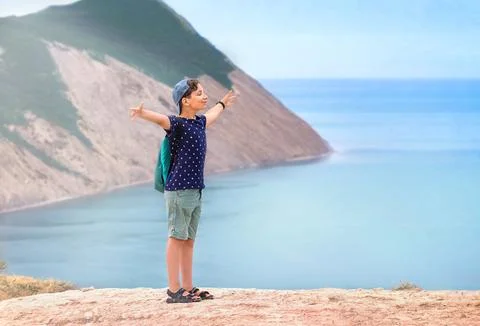 A 10-year-old boy with a backpack stands on the cliff of the mountain, joyf.. Stock Photos