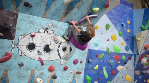 10-year-old boy climbing on an indoor bouldering wall with colorful holds Stock Footage 292016419