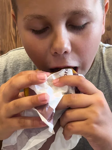 A 10-year-old boy eats a McDonalds burger with an appetite. Fast food and Stock Footage 314094961