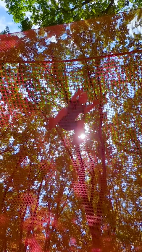A 10 year old boy plays in an outdoor net park, climbing a mesh maze and jumping Stock Footage 343617188