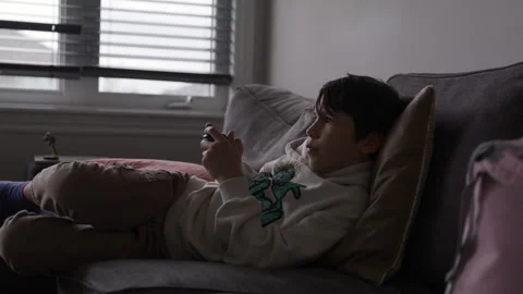 10 year old boy relaxing on couch playing video games - wide shot Stock Footage 316199315