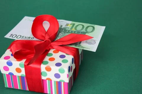 100 Euro banknote on a gift box with a red bow. Green background. Stock Photos