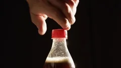 Man opens the plastic bottle of foamy cola against black background