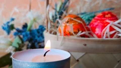 Burning candle, basket with Easter eggs, flowers