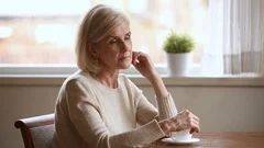Lonely mature woman sitting at table lost in sad thoughts
