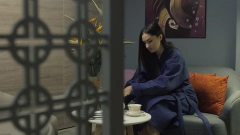 1080p video of a woman in blue robe pouring tea into a cup. Woman is sitting on Stock Footage