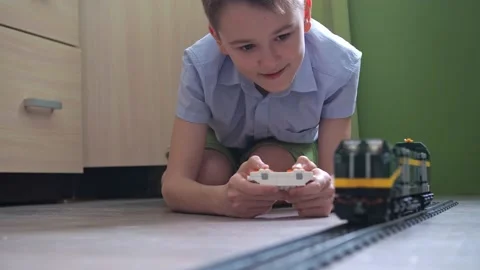 An 11-year-old boy is playing with a train on the controls on the floor in the Stock Footage 170447569