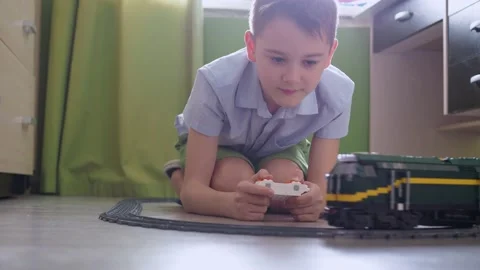 An 11-year-old boy is playing with a train on the controls on the floor in the Stock Footage 171129602
