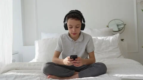 11 years old boy lies on the bed and listens to music with headphones 스톡 동영상 151346181