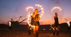 Fire show three women in their hands twist burning spears and fans in the sand