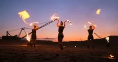 Fire show three women in their hands twist burning spears and fans in the sand