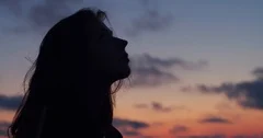 Dark profile of long-haired woman looking up to sky enjoying summer evening 