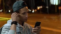 Multiethnic guy turn on music on his device, put on headphones and begins sleep