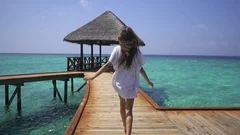 Lady in white dress runs on pier near water bungalows in the Maldives. Travel