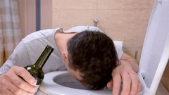 Man with nausea and vomit in toilet feeling hangover with wine bottle in hand.