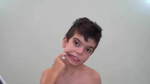 12 boy examines his forehead, teeth, cheeks, brunette, brown eyes Stock Footage 268429671
