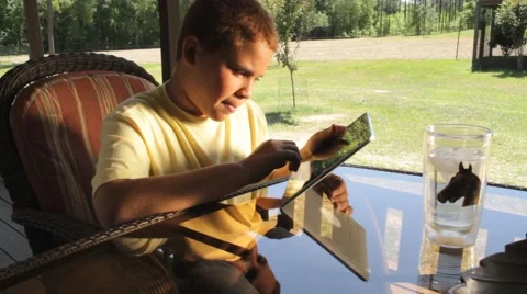 12 year old, mixed race boy writes and plays with iPad on a porch Stock Footage 45523350