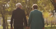 Back view of elderly couple holding hands while walking together in park .