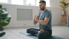 Slow motion of serious young man meditating at home moving hands in namaste
