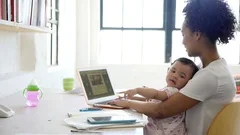 Mother working at laptop with baby daughter on lap in home office