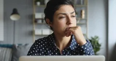 Thoughtful concerned indian woman working on computer thinking solving problem