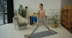 Young beautiful woman doing a warrior yoga pose (Virabhadrasana) at home