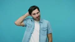 Frustrated confused young bearded guy in jeans shirt scratching head